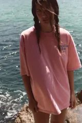 Camiseta oversize de manga corta y cuello redondo, color rosado con efecto lavado, con pequeño texto estampado en azul en el pecho.