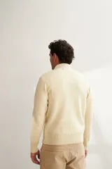 Campera tejida color marrón claro con cierre delantero, cuello alto y bolsillos delanteros. Tejida en 100% lana fina sin teñir.