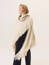 Triángulo de lana color beige con maxi flecos, diseñado por Margara Shaw en colaboración con Manos del Uruguay. Confeccionado con una mezcla de lana merino, mohair, viscosa, algodón y otras fibras, incluyendo lurex y un hilado teñido a mano con lentejuelas.