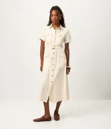 Vestido midi de sarga en color crudo, de manga corta, con diseño utilitario. Cuenta con cuello camisero, cierre frontal de botones, bolsillos con solapa en el pecho y en la falda, y cinturón ajustable con hebilla redonda en la cintura.