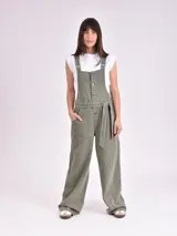 Monoprenda (jardinera) color verde oliva, de corte holgado y pierna ancha, con tirantes ajustables, cierre frontal de botones y lazo para ajustar en la cintura.