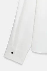 Camisa de cuello solapa y escote en pico, con manga larga y puños clásicos. Presenta un diseño con pliegues en el delantero y bajo asimétrico.