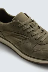 Zapatilla deportiva de estilo casual, confeccionada en una combinación de piezas de cuero con acabado de gamuza y paneles textiles. Presenta una horma redonda, cierre mediante cordones y una suela dentada en tono contrastante.