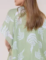 Kimono de gasa verde con estampado de hojas blancas y detalles de lurex. Presenta mangas cortas holgadas, diseño abierto al frente y terminación en punta con borlas en el ruedo.