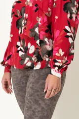 Blusa roja con estampado floral, escote en V con lazo en el cuello y mangas largas con frunces en los hombros.