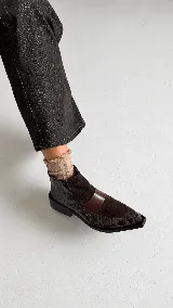 Bota corta de cuero con textura tipo reptil y paneles de gamuza en tono marrón oscuro. Presenta un diseño de punta cuadrada, cierre lateral y un taco cuadrado de madera.