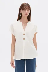 Blusa de viscosa color blanco, de corte holgado, con cuello en V y detalles de botones en el frente.