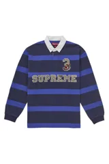Camisa de rugby Supreme de manga larga con diseño de rayas horizontales en tonos azul marino y azul eléctrico. Presenta cuello polo blanco, cierre frontal con botones ocultos y apliques bordados con el nombre de la marca y el número 3 en el pecho.