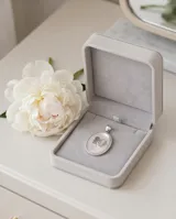 Dije ovalado de plata 925 con base de nácar, borde decorado con circonias y diseño central de nene y nena.