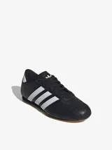 Zapatillas Adidas de cuero negro con las tres rayas blancas y suela color caramelo.