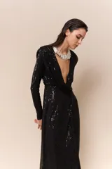 Vestido largo de lentejuelas color negro, con escote profundo en V, mangas largas y tajo lateral en la falda. Presenta un diseño cruzado con fruncido en la cintura y espalda elastizada.