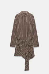 Vestido corto de estilo camisero con estampado de rayas verticales, cuello solapa, manga larga y cierre frontal con botones. Presenta un detalle de lazada en la cintura que crea un efecto drapeado y un bajo asimétrico.