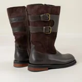 Bota de caña alta color chocolate, confeccionada en una combinación de cuero liso y gamuza. Presenta diseño con doble hebilla lateral, cierre con cremallera interna y tacón bajo con suela resistente.