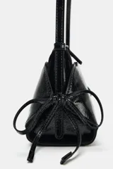 Bolso de hombro de material efecto acharolado negro, con doble compartimento exterior, cierre de cremallera y detalles de lazos en los laterales.