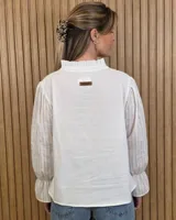 Blusa blanca de algodón con escote en V y cuello mao. Presenta mangas largas abullonadas con puños acampanados y fruncidos.