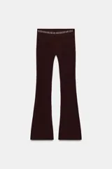 Pantalon negro de corte flare, confeccionado en tejido elastizado. Presenta tiro alto, cintura elastizada y detalle de tachas metálicas decorativas en la parte superior.