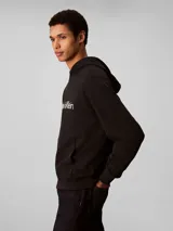 Buzo con capucha Calvin Klein de corte regular, confeccionado en mezcla de algodón regenerado y poliéster reprocesado. Presenta el logo de la marca estampado en el pecho, bolsillo tipo canguro frontal y terminaciones acanaladas en puños y cintura.
