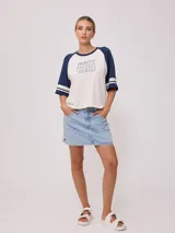 Remera bicolor Rusty de corte holgado y estilo deportivo, con cuerpo blanco y mangas raglán azules con doble raya blanca. Presenta estampado frontal con el texto 'RUSTY 85'.