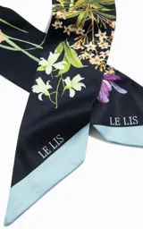 Pañuelo de forma rectangular con estampado floral sobre fondo azul oscuro y bordes en tono celeste claro, con el logo de la marca estampado en los extremos.