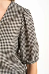 Blusa de algodón con estampado de cuadros vichy en tonos negro y blanco. Presenta escote en V, cierre frontal con botones y mangas cortas abullonadas con terminación elástica.