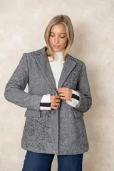 Blazer de corte sastre con diseño de espiga en tonos grises. Presenta un bordado floral lineal en el lateral, solapas clásicas, cierre frontal con un botón y bolsillos con solapa.