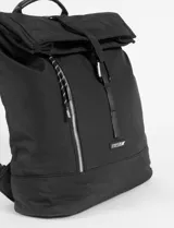 Mochila de tela negra con diseño de solapa superior y cierre de mosquetón. Cuenta con un bolsillo frontal vertical con cierre, asa superior y correas ajustables.