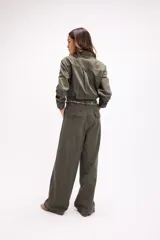 Mono de estilo utilitario color beige, con cierre frontal de botones, bolsillos en el pecho y cintura entallada con detalle de cadenas decorativas. Presenta mangas largas y piernas de corte recto y holgado.