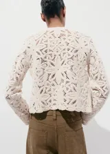 Chaqueta de punto grueso color beige con diseño de encaje en relieve, cuello redondo y cierre frontal.