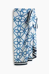 Pareo de playa en tejido liviano color blanco, con estampado geométrico de nudos y cuerdas en tono azul, y bordes con rayas azul marino.