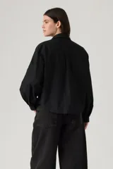 Camisa negra de manga larga con detalles bordados y calados en los hombros y el pecho. Presenta cuello clásico y cierre frontal con botones.