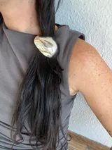 Colita de pelo con aplique metálico de diseño ovalado y acabado pulido brillante.