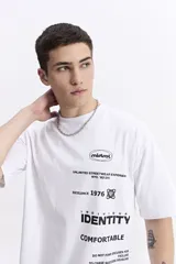 Remera blanca de manga corta con escote redondo y fit regular. Presenta múltiples estampados de texto y logos en color negro, incluyendo "mistral", "UNLIMITED STREETWEAR EXPERIENCE NYC. '83 DIV.", "EXCELENCE 1976", "INDIVIDUAL IDENTITY" y "COMFORTABLE".