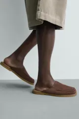 Zueco de piel con acabado serraje en color marrón, diseño sin talón, puntera redonda y detalle de costura tipo mocasín en el empeine.