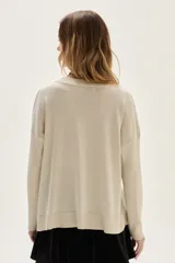 Sweater de tejido de punto con acabado brillante de lurex, escote en V y mangas largas. Presenta detalles de bordados florales en los hombros y un diseño con tajos laterales en el ruedo.