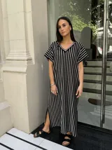 Vestido largo de tejido de punto con diseño de rayas verticales en blanco y negro. Presenta escote en V, mangas cortas y tajos laterales en el ruedo para mayor movimiento.