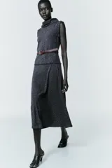 Vestido midi de tejido texturizado en color gris oscuro, con cuello alto fluido, diseño sin mangas y acabados deshilachados. Incluye un cinturón fino de cuero en color marrón con hebilla metálica y cierre de cremallera oculta en la espalda.