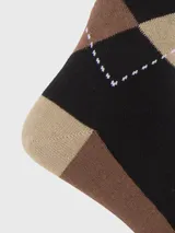 Calcetín de largo medio con diseño de rombos en tonos negro, marrón y beige. Presenta un pequeño bordado de perro en uno de los rombos.