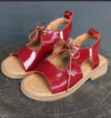 Sandalias rojas de cuero charol con puntera descubierta y cierre con cordones finos.