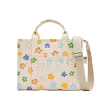 Bolso tote mediano de lona color crema con estampado de margaritas de colores. Tiene cierre superior con cremallera, asas superiores de lona y correa de cincha ajustable y extraíble.