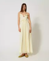 Vestido largo color amarillo pálido, confeccionado en georgette con rayas de raso. Cuenta con tirantes finos, escote de pico decorado con volantes y falda fruncida de corte redondeado en la cintura. Prenda forrada, de corte holgado.