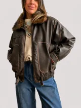 Campera estilo bomber de efecto cuero en color chocolate, con cuello de pelo sintético desmontable, cierre frontal, bolsillos laterales amplios y cintura elástica con ajuste lateral.