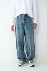 Jean de corte baggy con silueta holgada y relajada, confeccionado en denim de algodón con lavado azul clásico. Presenta diseño de cinco bolsillos, cintura con trabillas y cierre frontal con botón y cremallera.