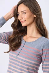 Remera de manga larga con cuello redondo y cierre frontal parcial con botones. Presenta un diseño de rayas horizontales en tonos pastel sobre una base beige, con aberturas laterales en el ruedo.