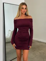 Vestido corto de color bordo, con diseño sin hombros y mangas largas. Presenta un ajuste entallado con detalle de frunces laterales en toda la falda.