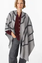 Ruana de tejido de punto con diseño geométrico abstracto en contraste. Presenta una caída fluida y abierta, ideal para superponer sobre otras prendas.