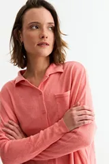 Cardigan de punto color salmón, con cuello tipo polo, cierre frontal de botones y bolsillo pequeño en el pecho. Presenta mangas largas con puños acanalados y un diseño de corte holgado.