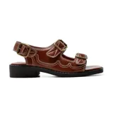 Sandalias bajas de cuero color marrón con pespuntes blancos y hebillas metálicas.