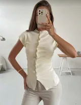 Top de tejido de punto color crema, con cuello alto, mangas cortas y cierre frontal asimétrico con botones y detalle de volados laterales.