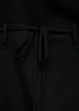 Vestido corto negro de diseño asimétrico con escote de un solo hombro y manga larga. Presenta un corte entallado con detalle de lazo ajustable en la cintura y cierre de cremallera lateral.