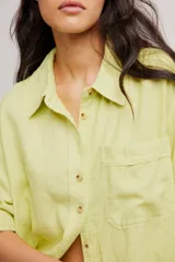Blusa de lino color blanco crudo, de corte relajado, con cuello clásico, cierre frontal de botones, bolsillo en el pecho y mangas largas con presillas para arremangar.